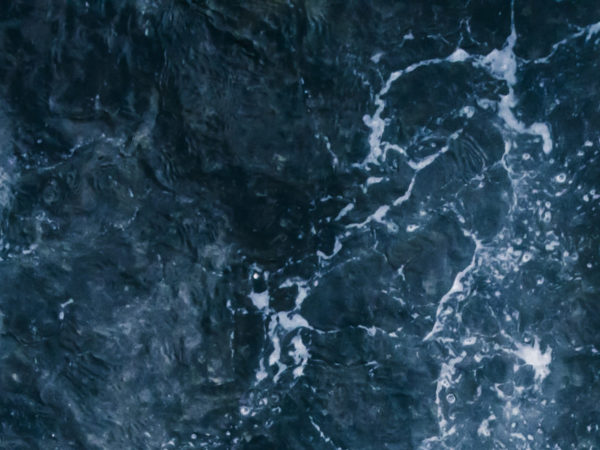 The blue surf of the sea with white waves, splash, foam and bubbles at high tide, aqua abstract background