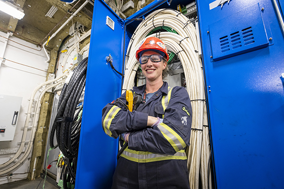 Woman in electrical room in full PPE smiling at camera