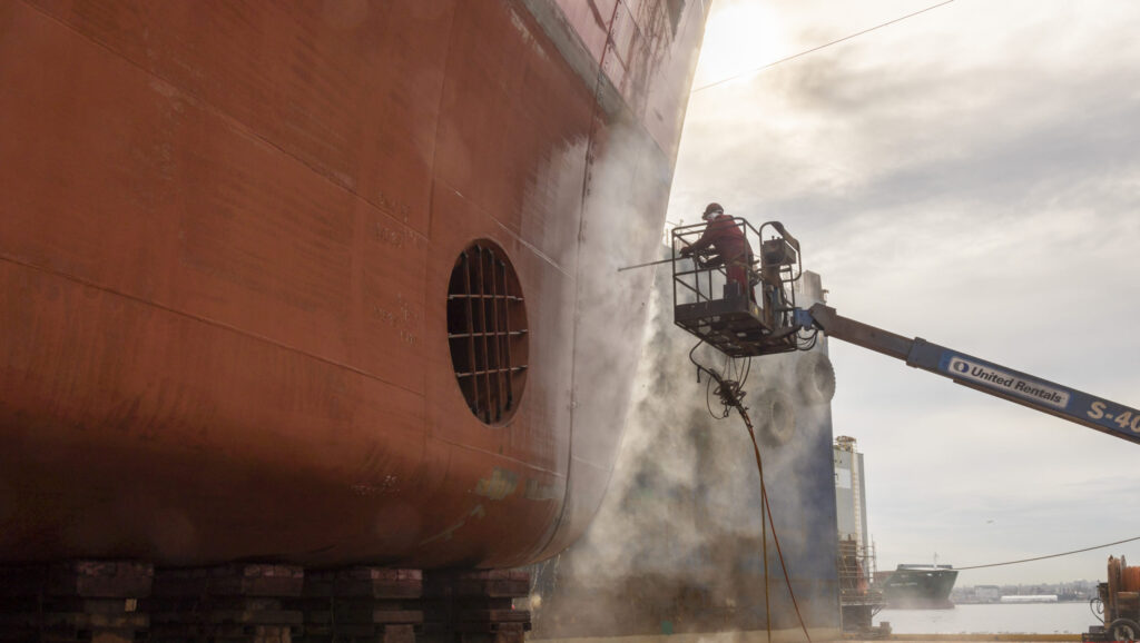 man spraying hull of ship