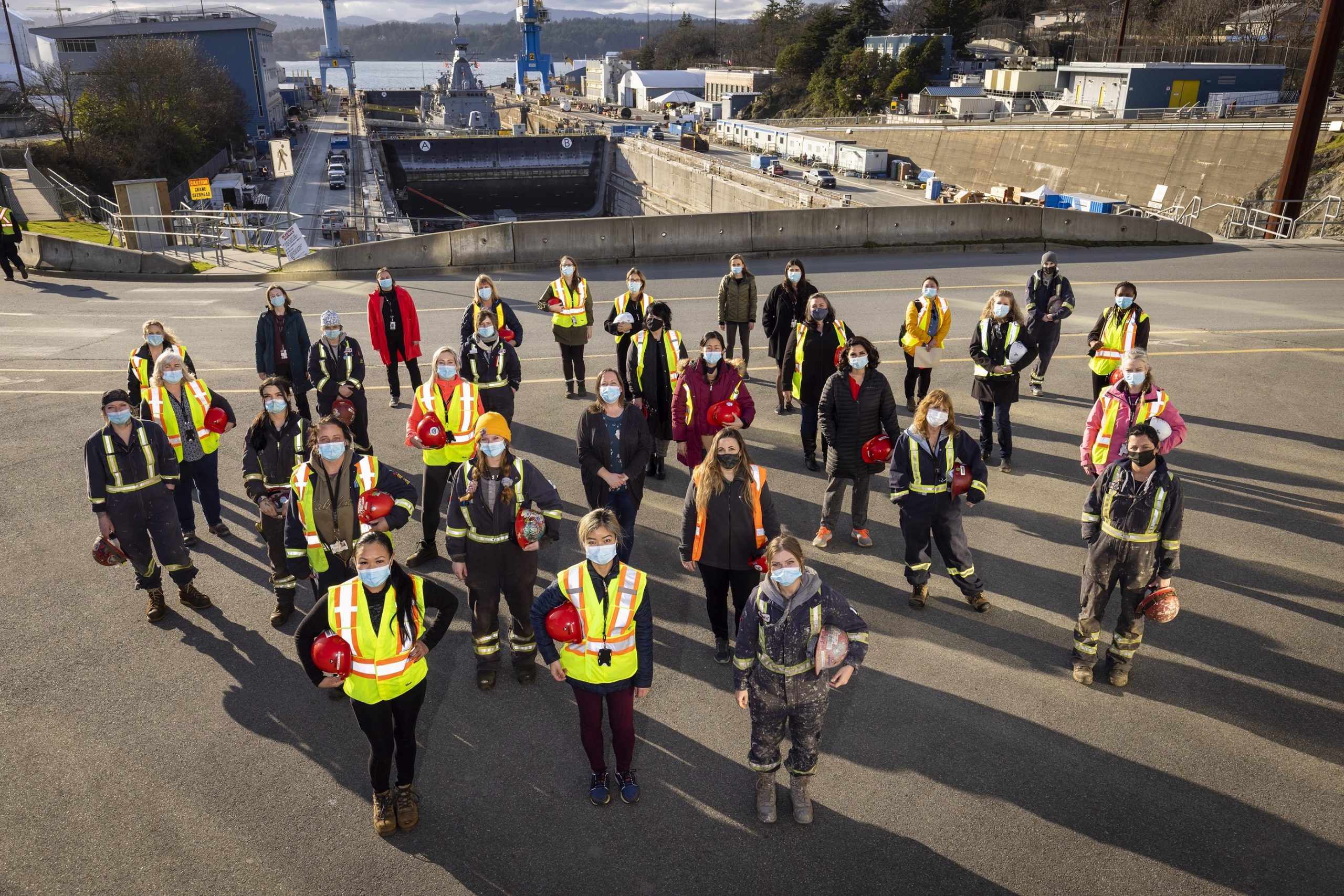 group of women in foreground. Victoria shipyards drydock in background. Navy ship in drydock
