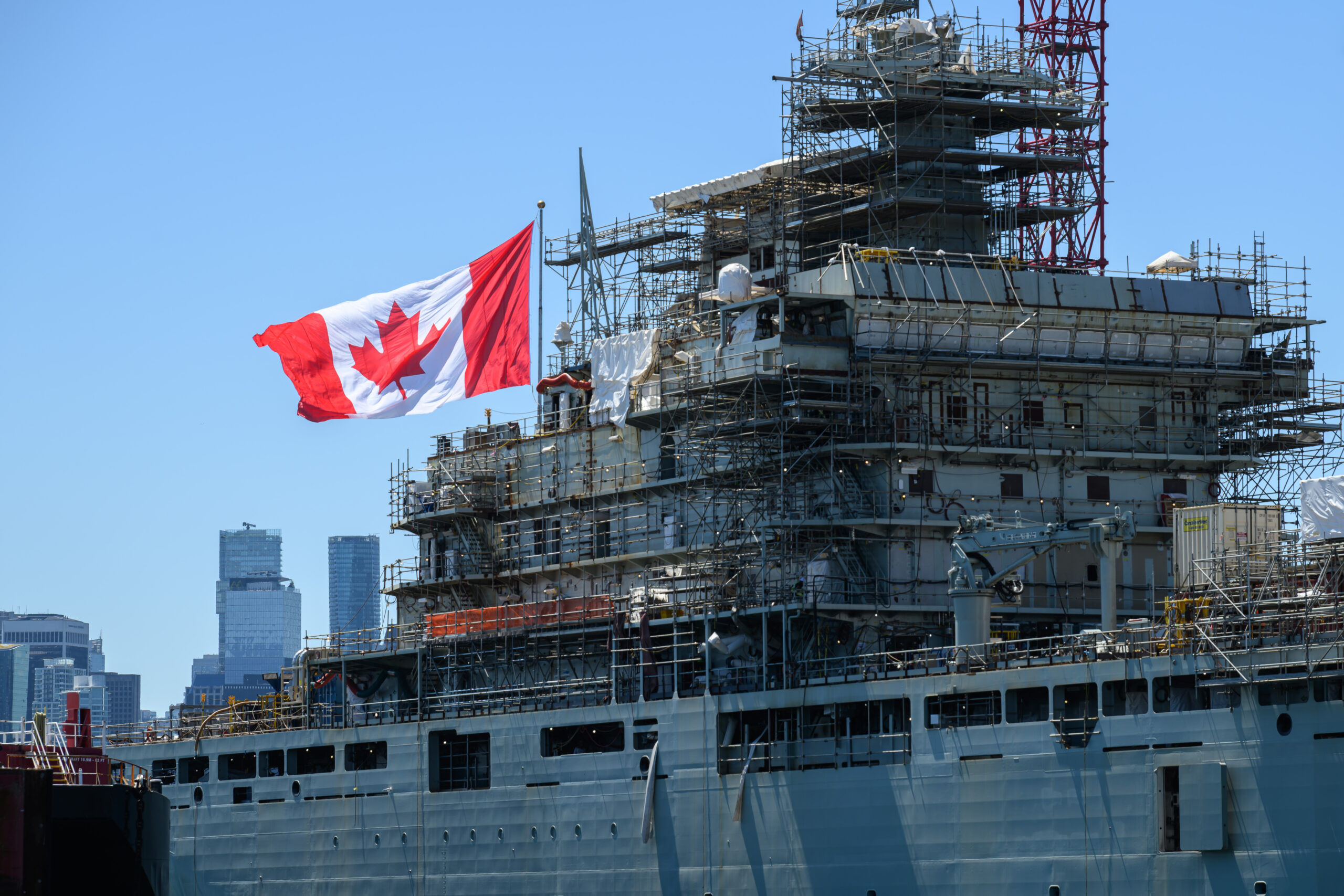 Large Canada flag waving behind a large navy vessel.