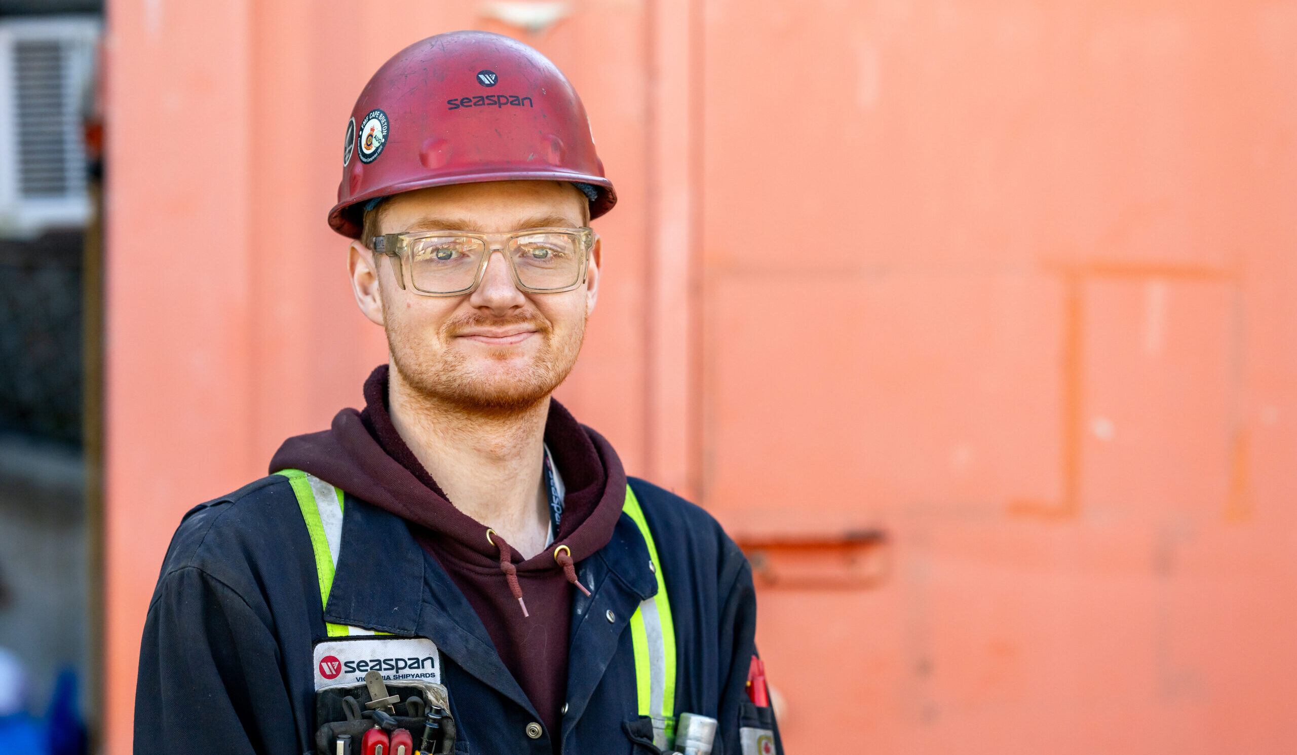 Victoria Shipyards employee standing in shipyard wearing red hard hat and coveralls