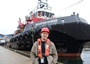 Christopher Sullivan stands in front of a tugboat, Seaspan Raider