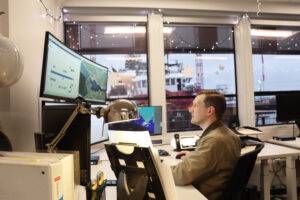 Christopher sits at his desk viewing large monitors
