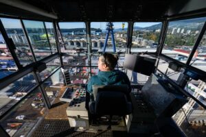 Crane operator sitting in the cabin of the crane, view of shipyard below. 