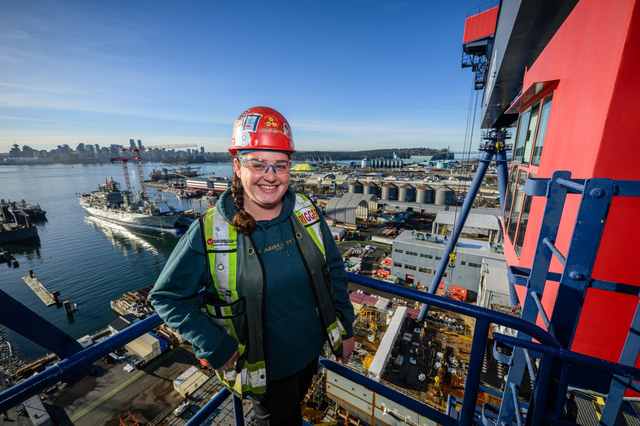 Woman smiling and wearing hard hat and high viz vest is shown standing on platform on Big Blue, an 80m high gantry crane in North Vancouver