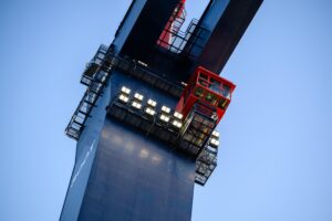 Photo looking up at the blue structure of the crane, focusing on the red crane operator's cabin. 