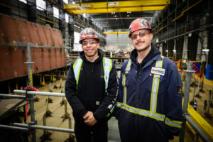 two welders stand side by side in coveralls and hard hats in Vancouver shipyards shop