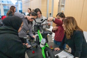 A team of women engineers assemble a green bike together
