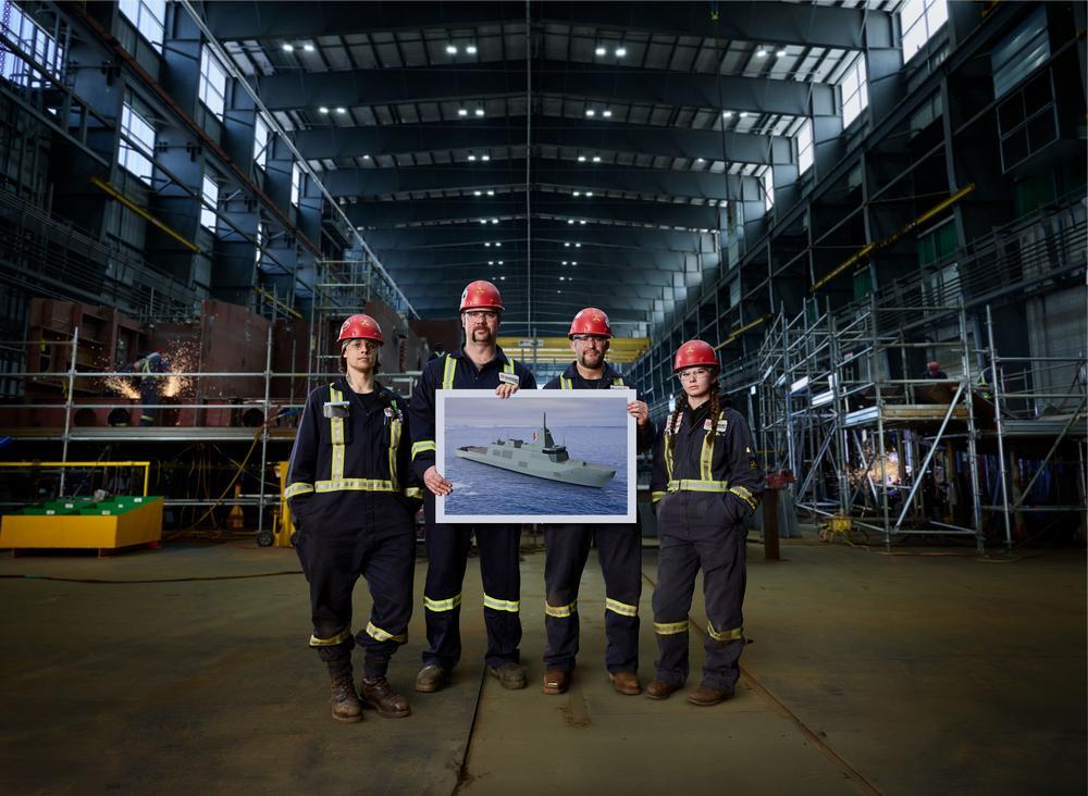 four shipyard workers hold an image of a corvette