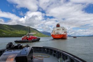 two red vessels in the ocean, one is a tugboat and one is a larger lng carrier