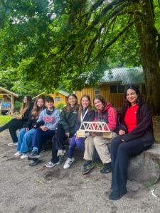 group of young girls at a summer camp holding a bridge made of popsicle sticks